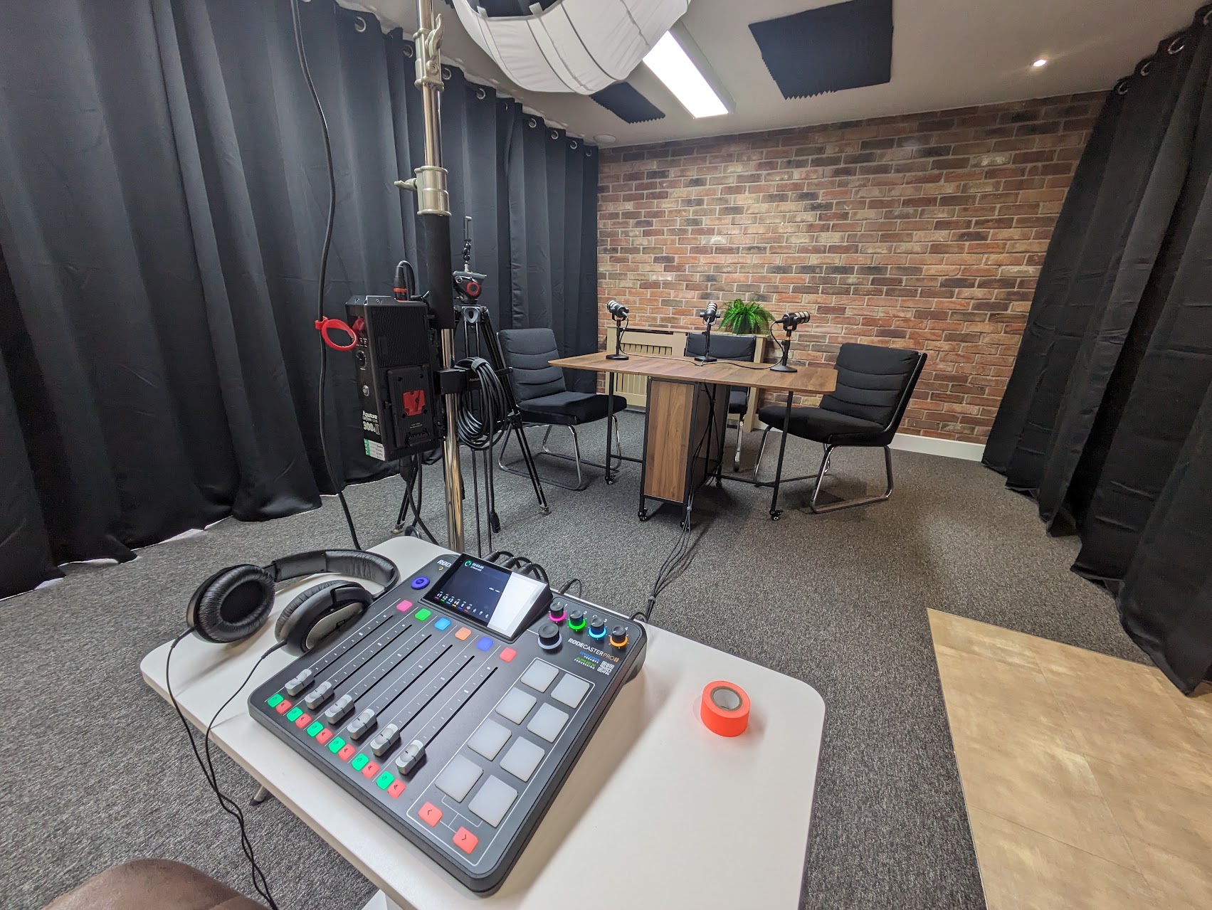 Brave New Beast podcast room with table, chairs, microphones, cameras and brick backdrop